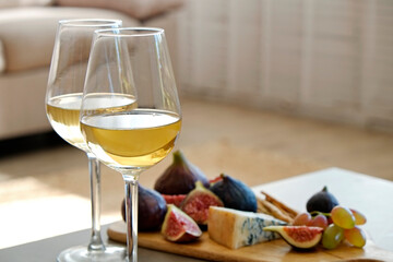 Two wineglasses of vintage chardonnay with delicious appetizers. Couple of glasses of white wine, italian breadsticks, figs and grapes. Interior background. Close up, copy space. - obrazy, fototapety, plakaty