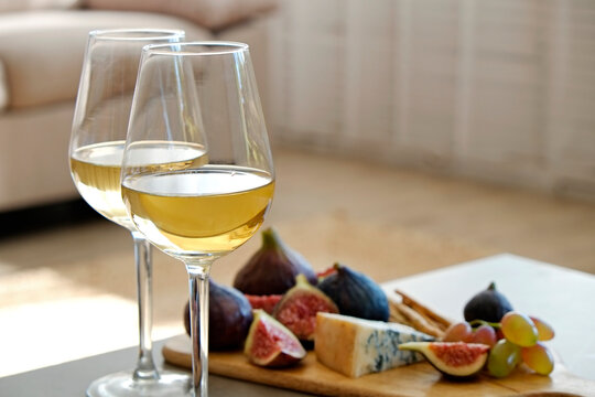 Two wineglasses of vintage chardonnay with delicious appetizers. Couple of glasses of white wine, italian breadsticks, figs and grapes. Interior background. Close up, copy space.