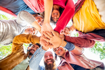 directly below portrait of happy diverse large group of multicultural friends holding hands making high five stacking them together outdoors. convivial people having fun. friendship, lifestyle concept - Powered by Adobe