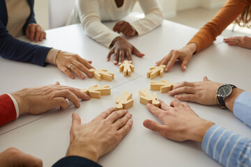 Fototapeta Group of multiethnic business people and teammates sitting around office table put little wooden human figures in circle as symbol of community, team, help, cooperation, collaboration and teamwork obraz