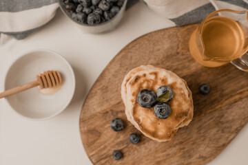 Pancakes with maple syrup and blueberries on wood on a light background, copy space. Summer homemade breakfast.