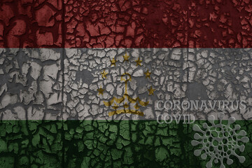 flag of tajikistan on a old metal rusty cracked wall with text coronavirus, covid, and virus picture.