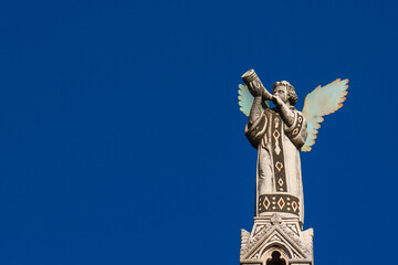 Cherub Angel blowing trumpet. A medieval 13th century statue a the top of St Michael Church in...