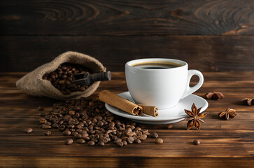 Black coffee with cinnamon in a white cup on a dark wooden table. Coffee beans in a canvas bag and stars of badyan in the background