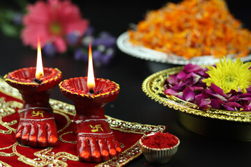 Clay Lamp Known As Diya, Deep, Diyo, Deepa Or Deepam WIth Goddess Feet Lakshmi Charan Illuminating On Red Cloth Asan With Roli Sindoor Flowers And Bokeh Effect. Shubh Deepawali And Laxmi Pooja Theme