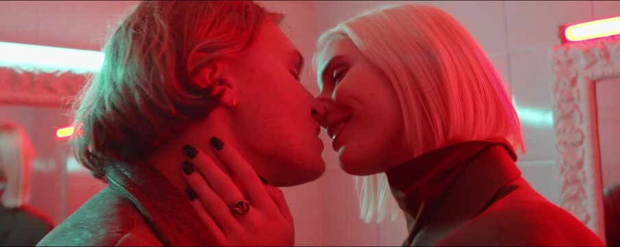 Zoom in shot of affectionate young couple kissing in room filled with red neon light