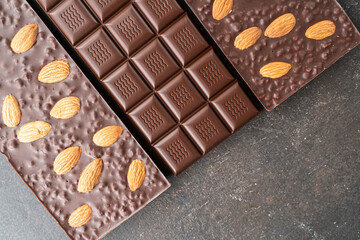 assortment chocolate bars with almonds, handmade sweets. Composition of bars milk and dark almond chocolate on black background, top view. Pastry craft on the table