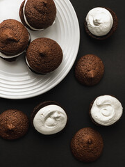 Chocolate sandwich cookies, baked biscuits stuffed with vanilla cream on a white plate on black background
