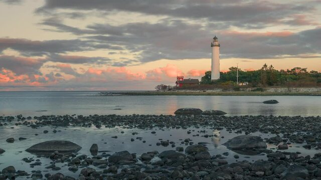 Time lapse of Swedish lighthouse Lange Erik on island in north of Oeland during sunset with dramatic moving clouds, stone coast in the front
