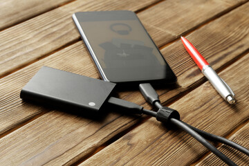 Pen and an external portable SSD connected to a smartphone on a rustic pine-board table. Portable Solid State Drive. The concept of modern technologies, ecology and gadgets. OTG interface