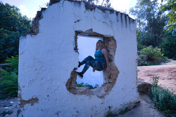 Young blonde woman in sportswear, doing calisthenics exercises in a window of a dilapidated building. Concept, calisthenics, fitness, exercise, curvy girl.