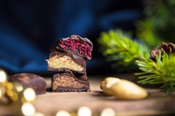 Close up of chocolate vegan candy bars with colourful fillings on wooden cutting board with cashews and Christmas holiday decorations 