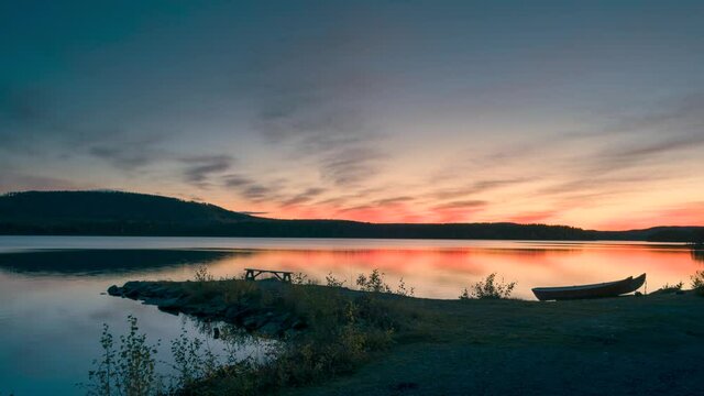 Time lapse of sunset at lake Stor-Skabram near Jokkmokk in North Sweden during sunset, moving colourful clouds in the sky, couple sitting on bench
