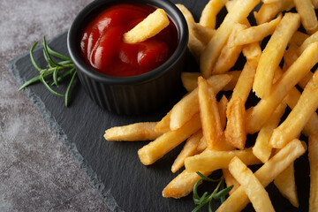 Homemade baked french fries with ketchup and rosemary on a black slate board
