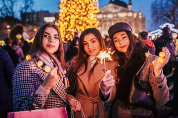 New Year. Women friends burning sparklers in Lviv by Christmas tree on street fair. Girls celebrating winter holidays