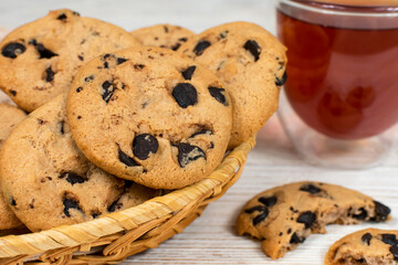 Chocolate cookies in a basket on the background of a glass cup of tea. Close-up.