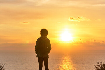 Hiker woman from behind looking at sunrise over the sea