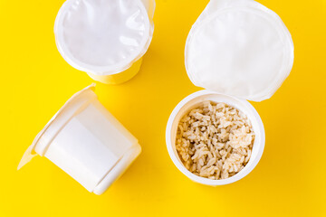 Selective focus to some plastic cups of pre-cooked microwave rice, one of them open, isolated on a yellow background.