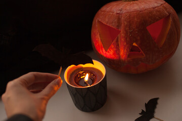 Hand holding a bat halloween decor near a candle and jack-o-lantern pumpkin decor