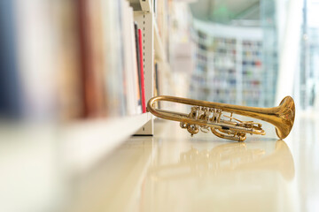 A raw brass rotary trumpet resting on a bookshelf in a library with a reflective floor