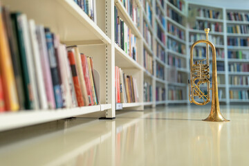 A raw brass rotary trumpet standing on its bell on a reflective light colored floor in the library with books and bookshelves © Janisphoto