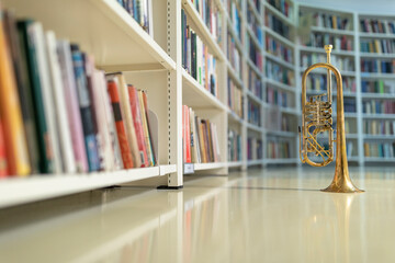 A raw brass rotary trumpet standing on its bell on a reflective light colored floor in the library...