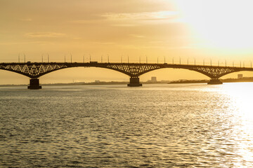 Bridge over a wide river in the rays of the setting sun.