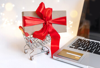 Shopping online during holidays. Beautiful gift for Christmas in shopping cart bought on the Internet. Store online, using a laptop and a credit card, christmas online concept