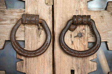 An old wrought iron door knocker on an old carved wooden door in the Russian style.  The forged handle of the handmade hammer is made of iron close-up against the background of a wooden door. 
