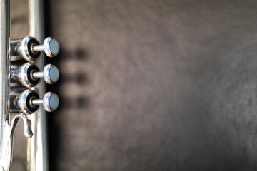 A part of a silver plated trumpet with its shadow on a brown table top. A brass instrument common to classical, jazz, pop, rock and other genres.