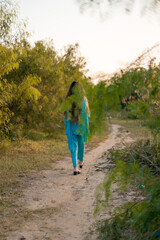 Girl in Pakistani dress walking on a path surrounded by greenery
