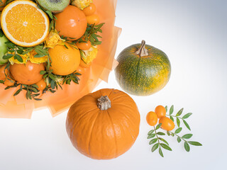Edible bouquet with tangerines and green apples for Halloween next to pumpkins. On a white background in the hands.