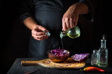 The cook pours olive oil into a fresh red cabbage salad. Cooking healthy food in restaurant kitchen on vintage table