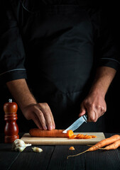 Obraz premium Cook is cutting carrots for vegetable soup in the restaurant kitchen. Close-up of the hands of the chef during work. Carrot diet
