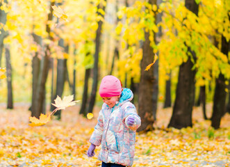 A 5-year-old girl in the autumn in a city park, having fun and throwing up yellow leaves fallen from the trees