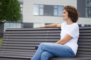 A 45-50 years old woman is sitting on a bench and resting.