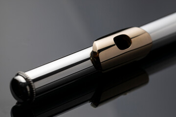 A silver plated head of a flute with a gold plated lip plate on a dark reflective surface