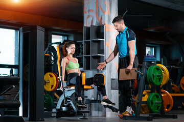 young woman exercising legs opening workout with personal trainer in gym