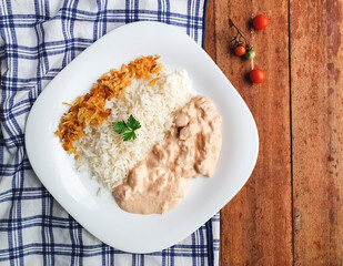 white plate with chicken stroganoff and straw potatoes on wooden background