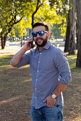 white man in casual attire and blue sunglasses texting in a park