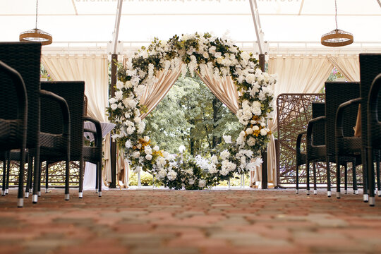 The round arch for the wedding ceremony is decorated with fresh white flowers and chairs for guests. Preparation for the wedding ceremony of the bride and groom. Wedding arch without people