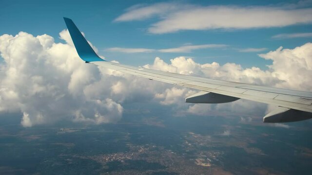 View of jet airplane wing from inside flying through white puffy clouds in blue sky. Travel and air transportation concept.
