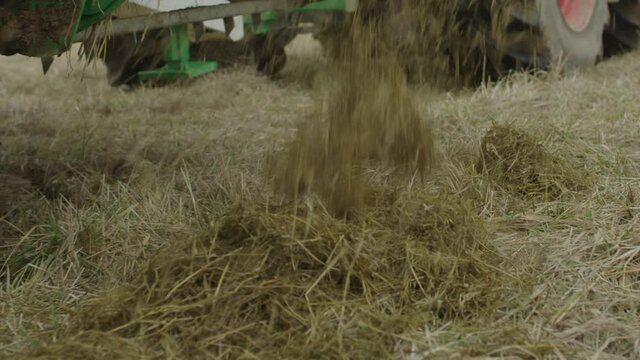Slow motion and close up tracking as farm equipment drops loose hay back onto a field into a windrow