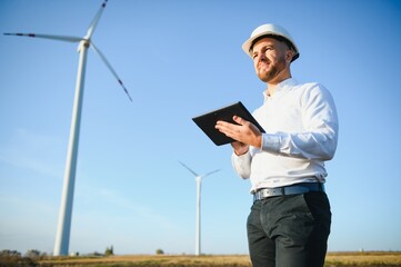 Young engineer man looking and checking wind turbines at field