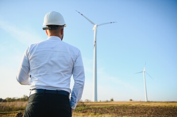 Young engineer man looking and checking wind turbines at field