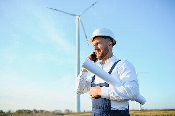 Engineer is checking energy production on wind turbine. Worker in windmills park in helmet.
