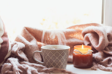 Cozy autumn or winter morning at home with cup of hot tea, candle, warm blanket and interesting book. Hygge home interior.