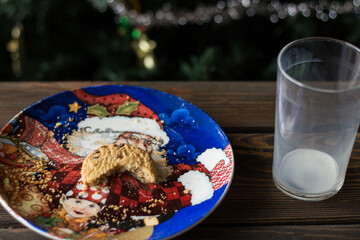 Bitten biscuit, crumbs and a empty glass of milk on a Christmas tree background.