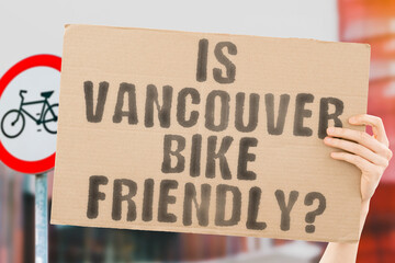 The question " Is Vancouver bike friendly? " on a banner in men's hand with blurred background. Transportation. Zero waste. Bicycle lane. Streets. City. Safety. Insecure. Road signs. Dangerous