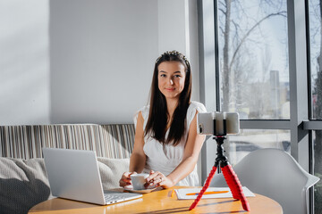 Obraz premium A young beautiful girl is sitting in a cafe, recording video blogs and chatting on social networks.